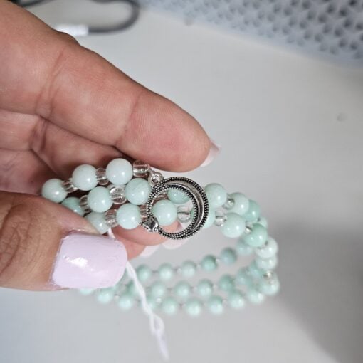 Hand holding a light green beaded bracelet with a silver circular clasp, on a white surface.