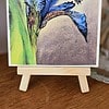 A detailed painting of a blue iris flower and a bee on a wooden easel, displayed on a wooden surface.