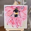 A watercolor painting of a bee on a pink flower is displayed on a small wooden easel.