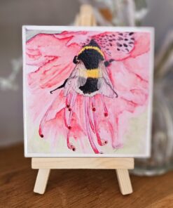 A watercolor painting of a bee on a pink flower is displayed on a small wooden easel.