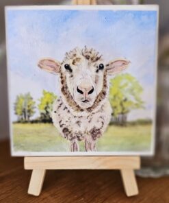 A small easel displays a painting of a sheep standing on green grass with trees and a blue sky in the background.