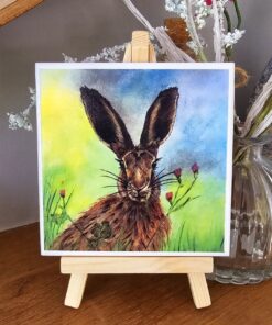 Watercolor painting of a rabbit on a small easel, with a colorful background and floral accents.