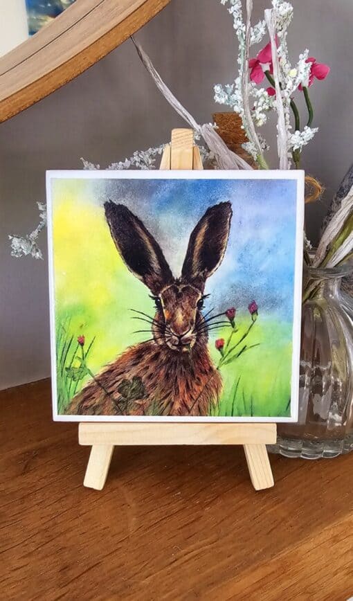 Watercolor painting of a rabbit on a small easel, with a colorful background and floral accents.