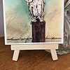 Watercolor painting of a barn owl perched on a wooden post, displayed on a small easel.