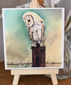 Watercolor painting of a barn owl perched on a wooden post, displayed on a small easel.