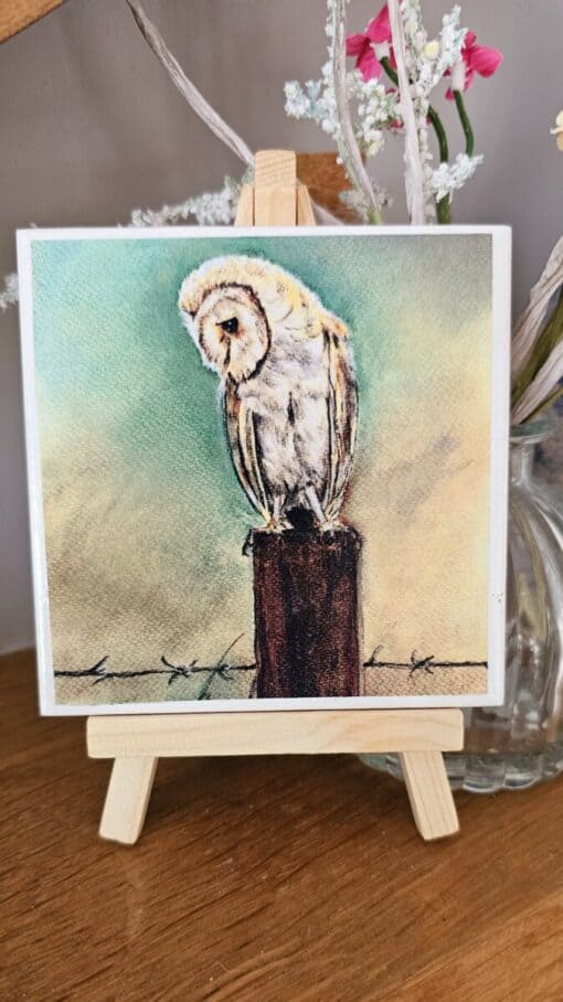 Watercolor painting of a barn owl perched on a wooden post, displayed on a small easel.