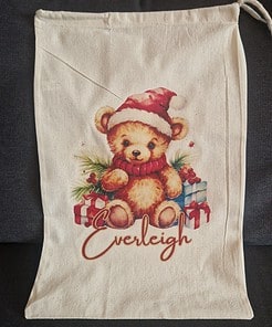 Personalised drawstring Christmas backpack with a cute teddy bear in a Santa hat, surrounded by gifts, and the name 