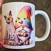 White mug featuring a gnome with a rainbow hat and butterflies, next to a letter "A" and the name "Alan.