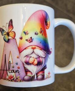 White mug featuring a gnome with a rainbow hat and butterflies, next to a letter "A" and the name "Alan.