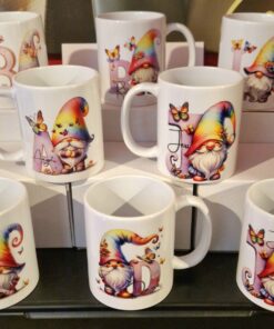 Colorful mugs featuring gnomes with rainbow hats and butterflies, each personalizable with a different letter.