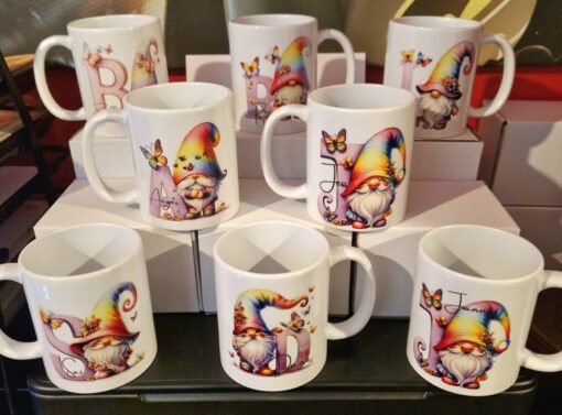 Colorful mugs featuring gnomes with rainbow hats and butterflies, each personalizable with a different letter.