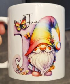 White mug with a colorful gnome, rainbow hat, butterflies, and the word "Jan" in cursive beside a decorative letter "J".