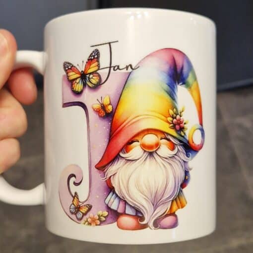 White mug with a colorful gnome, rainbow hat, butterflies, and the word "Jan" in cursive beside a decorative letter "J".