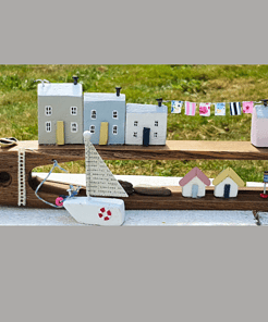 Handcrafted wooden model of a coastal village with small houses, a sailboat, and colorful clotheslines, set on grassy background.