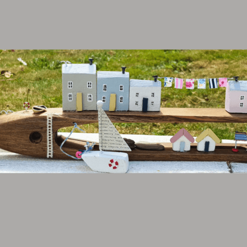 Handcrafted wooden model of a coastal village with small houses, a sailboat, and colorful clotheslines, set on grassy background.