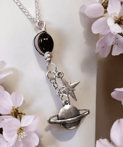 Silver necklace with star, moon, and planet charms hanging among light pink flowers.