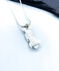 Silver pendant shaped like a rocket on a chain, placed on a white surface with a dark stone background.