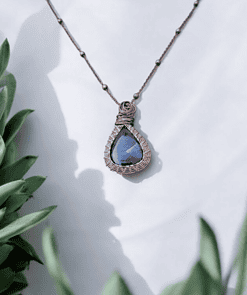 Bronze wire-wrapped necklace with a teardrop-shaped blue stone, framed by green succulent plants.