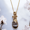 Gold necklace with an intricate pendant featuring a tree design, surrounded by white flowers on a light background.