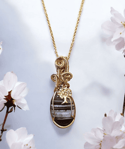 Gold necklace with an intricate pendant featuring a tree design, surrounded by white flowers on a light background.