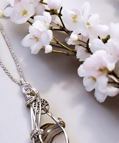 Silver wire-wrapped pendant with a striped stone, set against white and pink cherry blossom flowers on a light background.