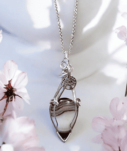 Silver necklace with an intricate pendant featuring a striped stone, surrounded by light pink flowers.