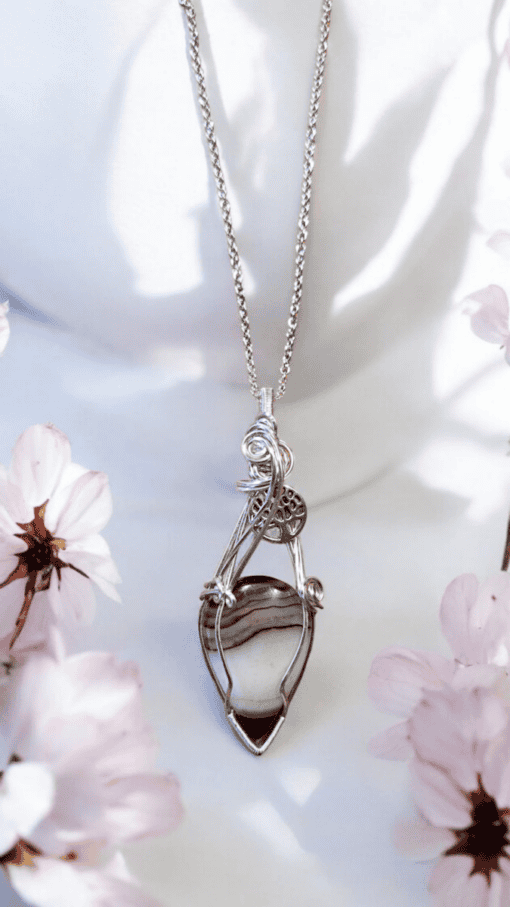 Silver necklace with an intricate pendant featuring a striped stone, surrounded by light pink flowers.