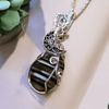 Silver necklace with a striped pendant, featuring intricate wire designs and a moon motif, surrounded by green succulent plants.