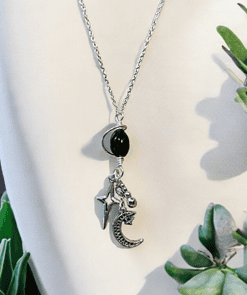 Silver necklace with a black bead and celestial charms, including a star, moon, and ball, displayed against a white background.