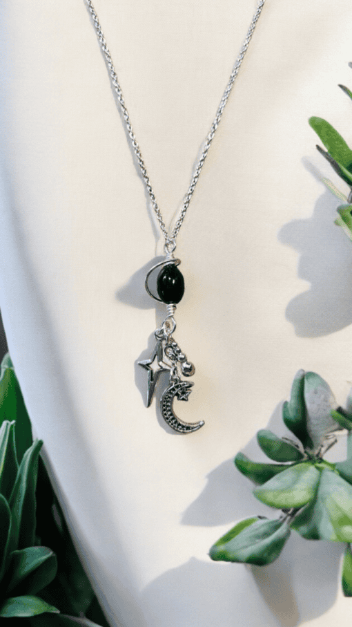 Silver necklace with a black bead and celestial charms, including a star, moon, and ball, displayed against a white background.