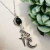 Silver necklace with star and crescent moon charms on a light background, surrounded by green succulent plants.