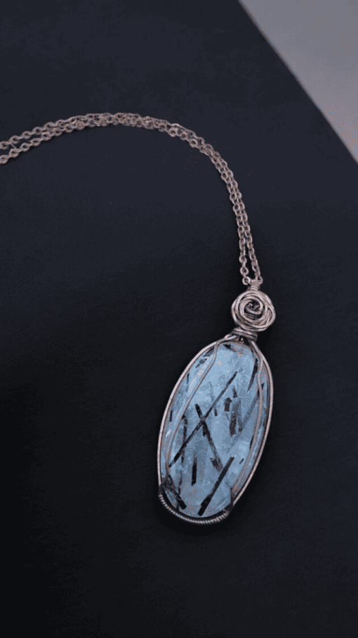 Pendant with an oval blue gemstone and delicate black streaks, wrapped in copper wire, on a matching copper chain.