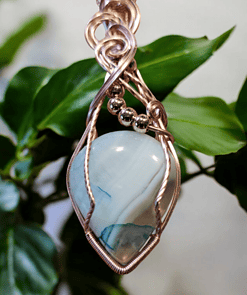 Silver wire-wrapped pendant featuring a blue gemstone and silver beads, with green leaves blurred in the background.