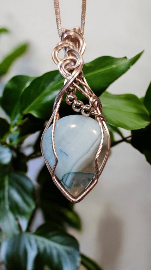 Silver wire-wrapped pendant featuring a blue gemstone and silver beads, with green leaves blurred in the background.