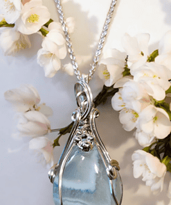 Silver pendant with a blue gemstone, surrounded by white flowers on a white background.