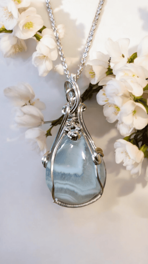 Silver pendant with a blue gemstone, surrounded by white flowers on a white background.