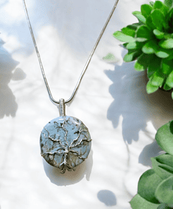 Silver tree of life pendant on a chain, surrounded by green succulent plants on a light background.