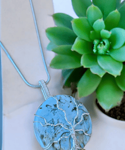 Round turquoise pendant with a silver tree wire-wrapped design, displayed next to a green succulent plant.