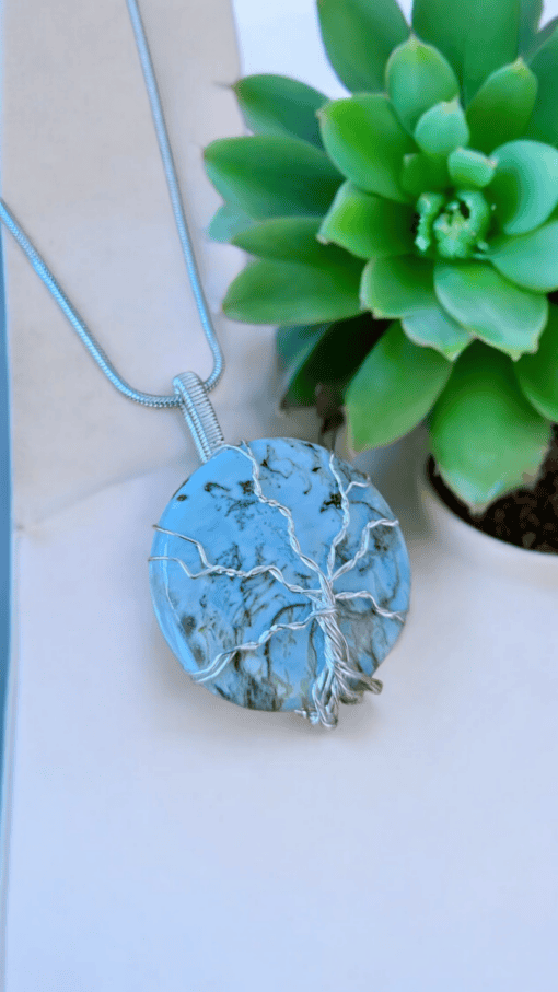 Round turquoise pendant with a silver tree wire-wrapped design, displayed next to a green succulent plant.