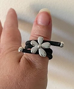 Silver flower ring with a black band worn on a thumb against a neutral background.