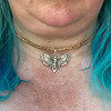 Close-up of a silver moth pendant necklace worn on a person with blue hair.