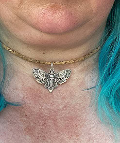 Close-up of a silver moth pendant necklace worn on a person with blue hair.