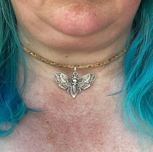 Close-up of a silver moth pendant necklace worn on a person with blue hair.