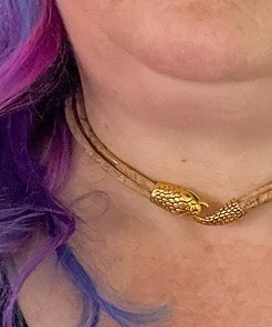 Close-up of a person wearing a beige choker necklace with a gold dragon clasp, and purple and pink hair peeking through.