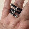 A hand wearing a ring made of three parallel black bands with silver beads and end caps.