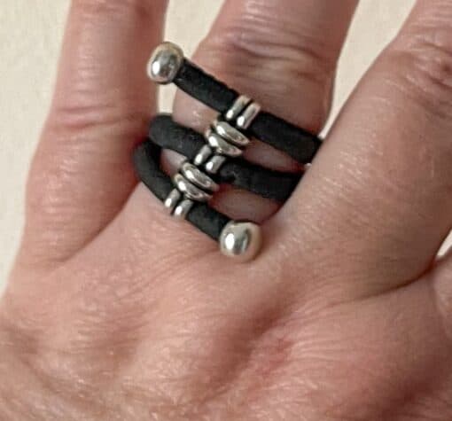 A hand wearing a ring made of three parallel black bands with silver beads and end caps.