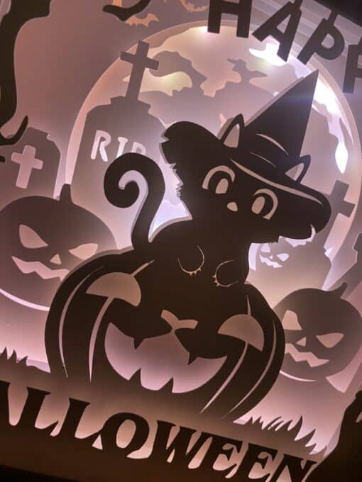 Silhouette of a black cat wearing a witch hat sitting on a jack-o'-lantern with "Happy Halloween" text and tombstones in the background.