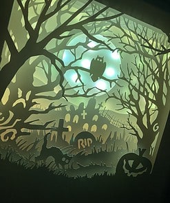 Silhouetted haunted graveyard scene with an owl on a tree, tombstones, black cat, and carved pumpkin, all under a glowing moon.