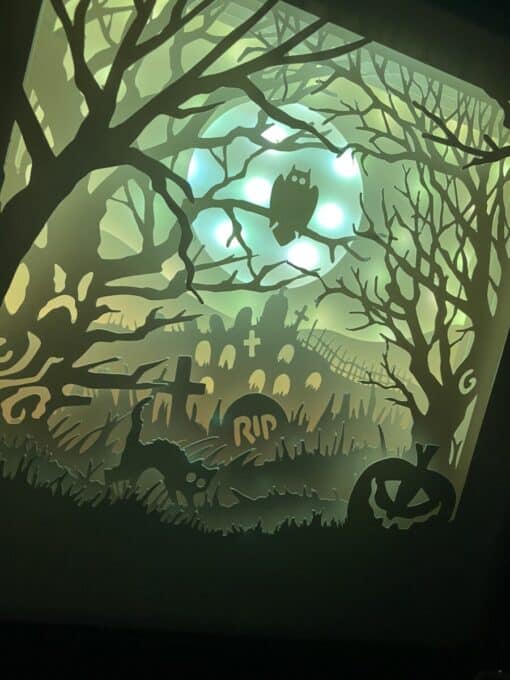 Silhouetted haunted graveyard scene with an owl on a tree, tombstones, black cat, and carved pumpkin, all under a glowing moon.