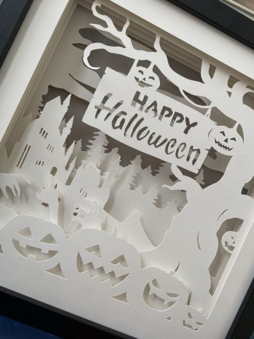 Paper art with a Halloween theme, featuring jack-o'-lanterns, a haunted house, ghostly hands, and a "Happy Halloween" sign.